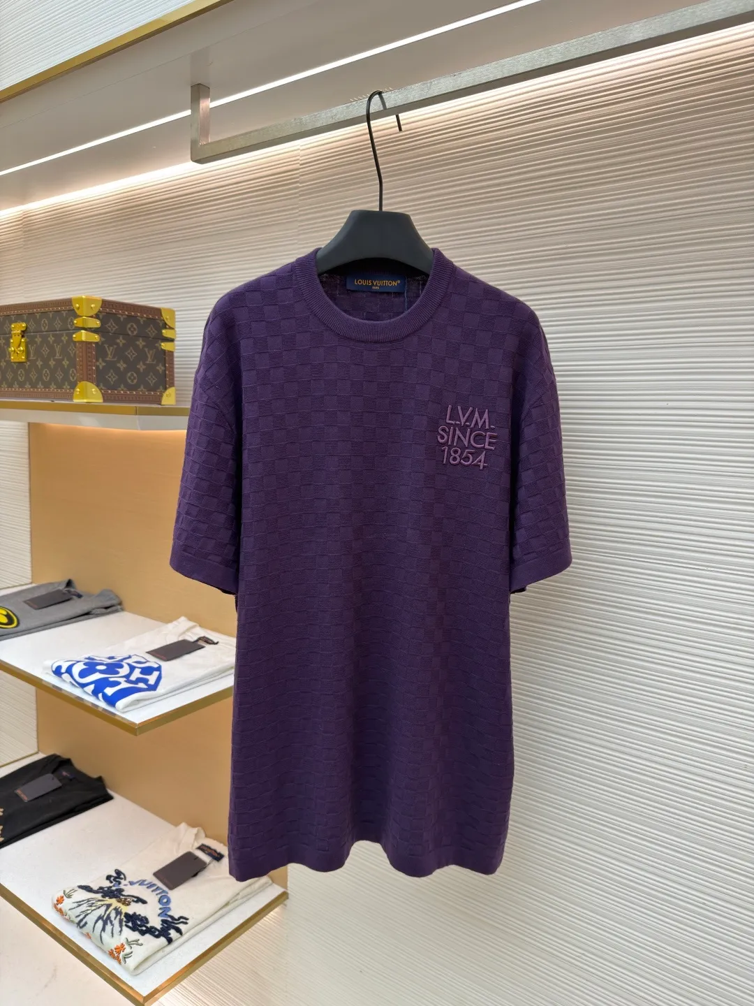 LOUIS VUITTON letter embroidered dark checkerboard jacquard short sleeves ●Original version: Purchased and developed at 9350 ●Item number: 1682319-B00 ●Fabric: 100% cotton ●Technology: jacquard knitting ●Color: Purple ●Version: Fitted version ●Weight: about 340 grams ●Size: S-M-L-XL ●Description: This Louis Vuitton purple knitted short-sleeve is made of custom worsted wool blended fabric. It is created with an 18-needle high-density weaving process using a computerized flat knitting machine to create a three-dimensional checkerboard texture. The checkered pattern is laser positioned and patterned. The size and spacing of each grid are accurate to 0.1 cm, showing a regular relief texture. The left chest uses same-color inlay embroidery technology, and the "LVM SINCE 1854" logo is embroidered with a high density of 1200 stitches/square centimeter. The embroidery thread is made of high-elastic mercerized cotton thread of the same color as the body, forming a natural texture layer with the knitted base. The neckline adopts seamless cylindrical rib technology, which is not easy to loose after high-temperature shaping treatment. The shoulders are made of seamless bonding technology to reduce the abruptness of the seams. The overall micro-profile tailoring combined with the invisible stitching technology of the side seams not only ensures the comfort of wearing, but also makes the body lines smoother. Each process has undergone multiple quality control tests by the brand to ensure the quality and durability of the craftsmanship. The overall wiring is straight and delicate, the fabric is comfortable and soft, and the color is consistent without color difference. It can be matched with the same style to create a fashionable look and control various occasions. Customized accessories, complete with three standards, same style for men and women!
